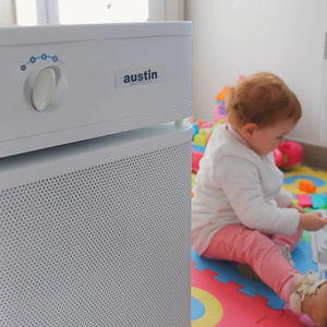 Baby playing on a colorful mat next to an Austin air purifier