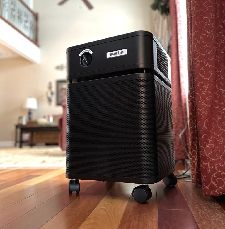 Black Austin air purifier on a wooden floor with a blurred living room background