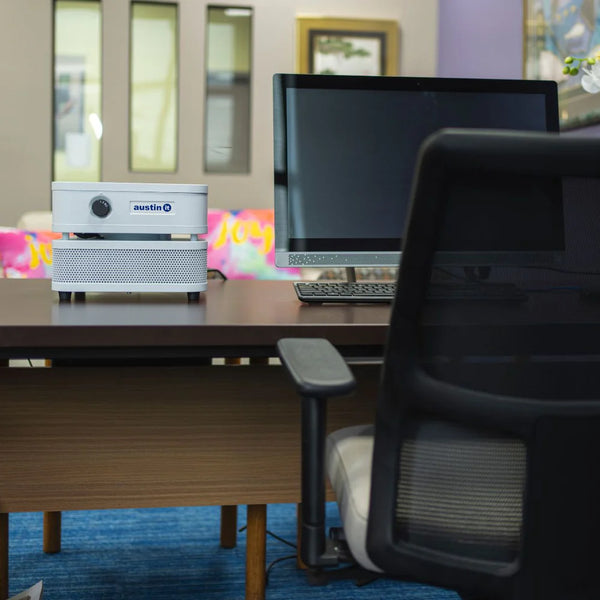 Office desk with computer setup, chair, and colorful decorations in the background with white air purifier