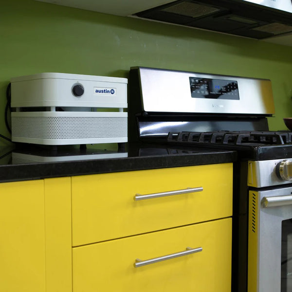Kitchen with yellow cabinets, black countertop, stainless steel appliances and personal sized air purifier on countertop 