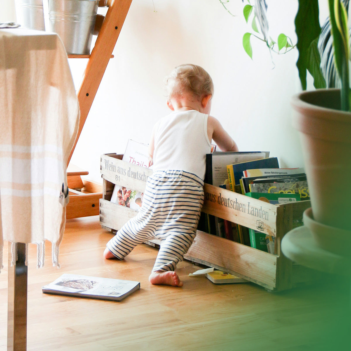 Child playing with books in a wooden crate on a wooden floor.