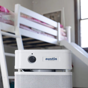 White air purifier with 'austin' branding on a blurred background of a room with bunk beds.